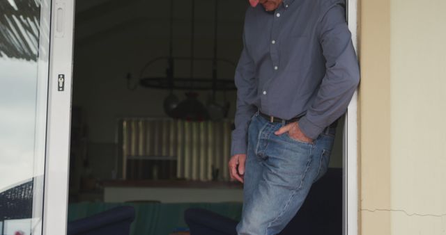 Middle-aged man wearing casual clothes, standing in a doorway, looking down thoughtfully. Impression of a relaxed, pensive mood. This image may be used for lifestyle blogs, articles on introspection, or casual fashion content.