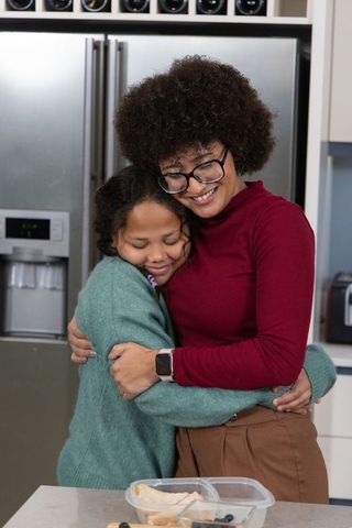African american mother hugging daughter in modern kitchen, sharing warm family moment