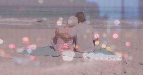 Senior couple sitting closely, gazing at ocean waves while enjoying a tranquil moment on a sandy beach. The calming ambiance and gentle waves complement the sense of serenity and relaxation, perfect for depicting romantic getaways, retirement, or lifestyle content promoting peaceful living and togetherness.