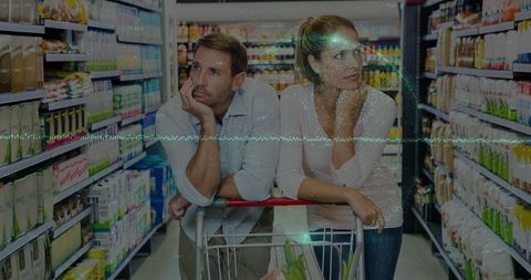 Couple leaning on shopping cart in supermarket aisle contemplating grocery choices