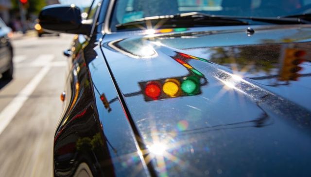 Glossy black car hood reflecting red yellow green traffic lights and lens flare