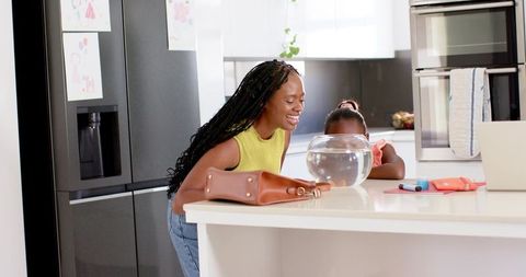 African american mother and daughter bonding over fishbowl on minimalist kitchen island