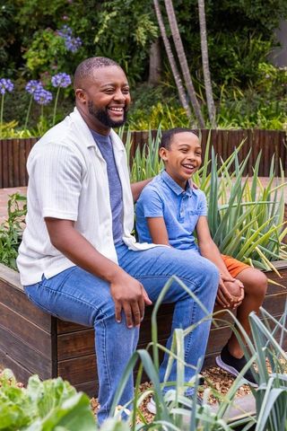 African american father and son laughing together in sunny backyard garden