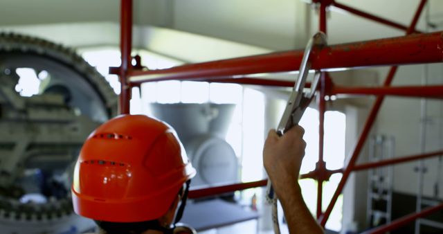 Image of a construction worker in an industrial site adjusting a scaffold with a wrench. Worker is wearing a safety helmet, ensuring workplace safety. Ideal for use in articles or brochures on construction safety, industrial maintenance, or promoting construction tools and equipment.