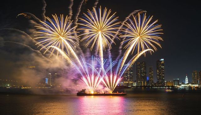 Golden blue fireworks exploding over waterfront from barge with vibrant night reflections