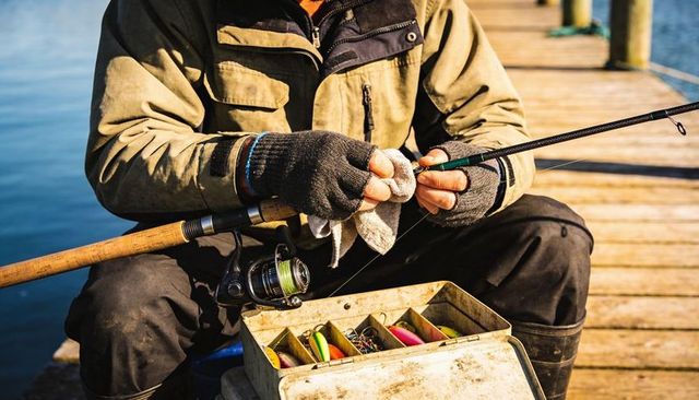 Angler preparing fishing rod on sunlit dock with tackle box and spinning reel