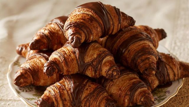 Stacked chocolate-drizzled croissants on vintage floral plate, golden buttery flaky layers
