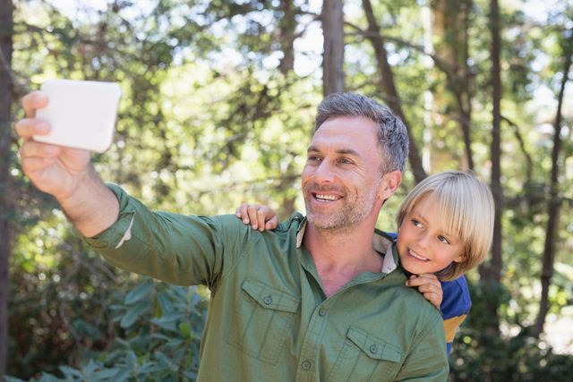 Smiling father and son taking selfie with mobile in forest