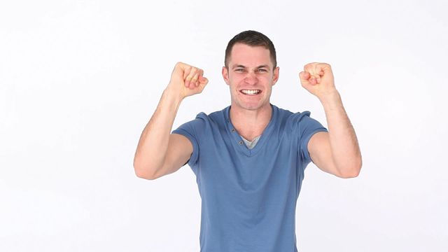 Cheerful man with raised fists celebrating success against a white background. Can be used for themes including success, achievement, celebration, enthusiasm, and positive emotions. Ideal for marketing materials, advertisements, websites, or social media pertaining to joyful announcements or winning moments.