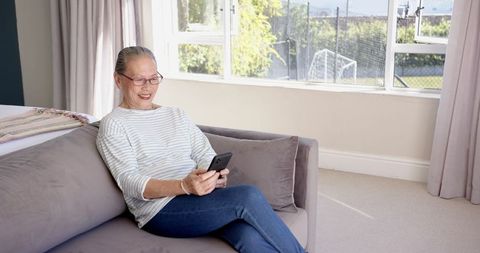 Senior Asian Woman Relaxing on Couch Using Smartphone