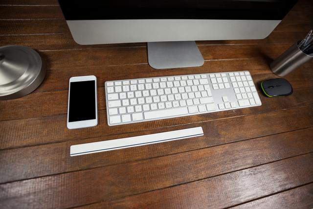 Modern office desk featuring a computer, mobile phone, keyboard, and mouse on a wooden surface. Ideal for illustrating contemporary workspaces, technology use in business, and productivity settings.