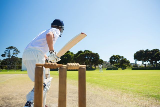 Cricket player in action, batting on a sunny day. Ideal for sports-related content, advertisements for cricket gear, or promoting outdoor activities and team sports.