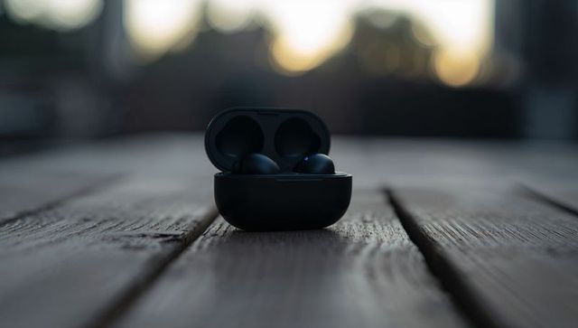 Black true wireless earbuds charging inside open case resting on weathered wood deck at dusk