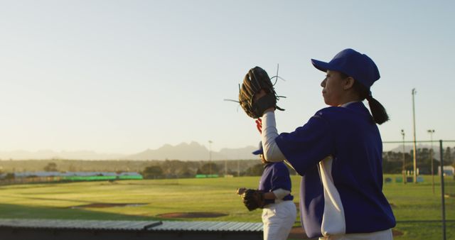 This image shows a female baseball player catching a ball in a glove during a game at sunset. Perfect for promoting women's sports, teamwork, and athleticism, as well as portraying outdoor activities and healthy lifestyles. Ideal for use in sports-related content, women's fitness brands, and inspirational stories.
