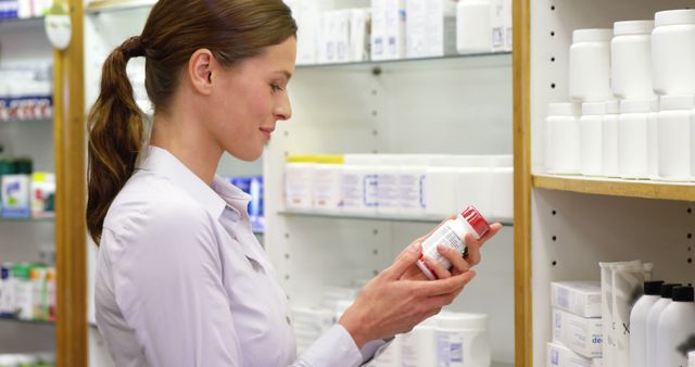 Professional pharmacist reading prescription label on medicine bottle in a pharmacy. Useful for healthcare promotions, pharmacy advertisements, articles on pharmaceutical industry, and educational materials for pharmacists in training.
