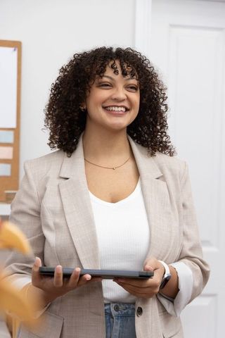 Smiling african american businesswoman holding tablet near corkboard in modern office