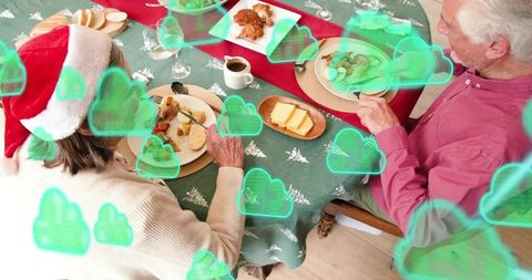 Senior couple enjoying christmas dinner carving roast, santa hat and green cloud overlays