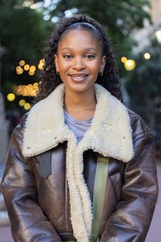 Young african american woman wearing shearling jacket smiling under urban string lights
