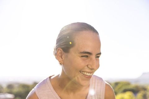 Smiling young woman squinting in bright sunlight with lens flare and natural green bokeh