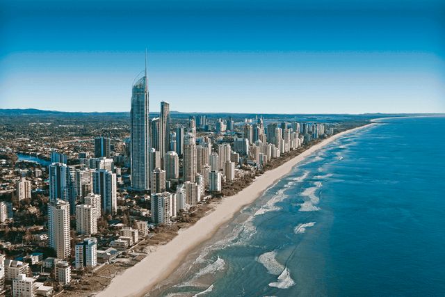 A breathtaking aerial view showcasing the skyline of Gold Coast, Australia. The image captures towering skyscrapers along the coast with blue ocean waves gently meeting the sandy beach. Suitable for use in travel and tourism promotions, Australian destination features, urban development showcases, or real estate marketing.