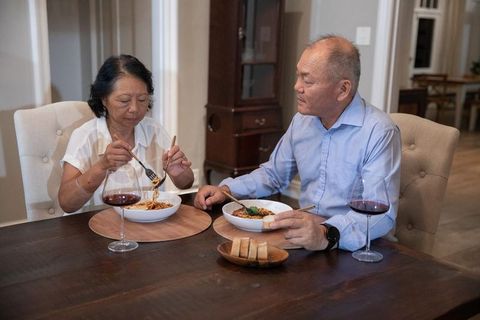 Asian couple sharing cozy homemade pasta dinner with red wine on rustic wooden table