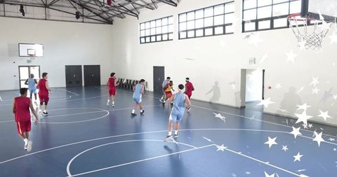 High school basketball teams dribbling in scrimmage on indoor blue court with daylight