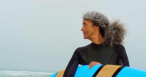 Active senior woman surfing on misty beach with surfboard