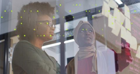 Diverse businesswomen collaborating in office with glass panel ideas