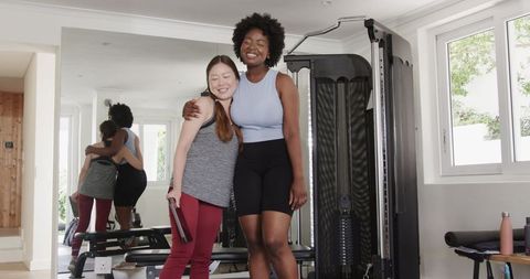 Diverse friends embracing while reviewing workout plan in modern gym
