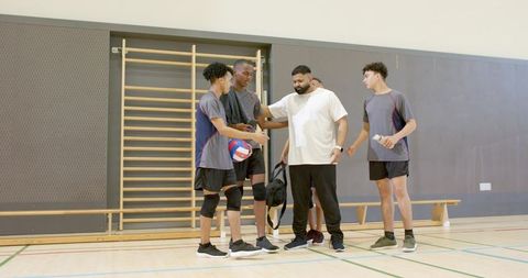 Coach giving pep talk to multiracial male volleyball team in indoor gym for teamwork training