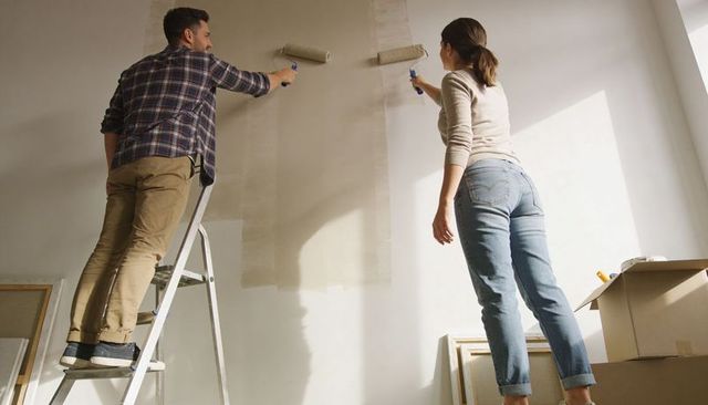 Couple Painting Interior Wall Together Using Rollers and Ladder for DIY Home Renovation