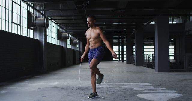 Muscular man jump roping inside a spacious, industrial-style gym. Perfect for use in fitness magazines, workout apps, health blogs, gym promotions, and articles on exercise routines and athletic training.