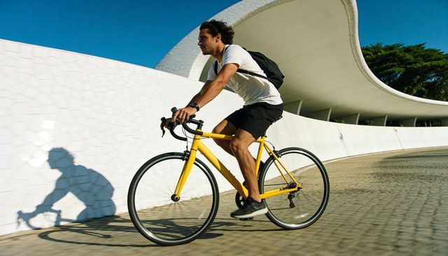 Young man riding yellow road bike along curved white mosaic wall under bright sky