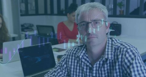 Senior analyst studying financial charts in open office with laptops and team collaboration