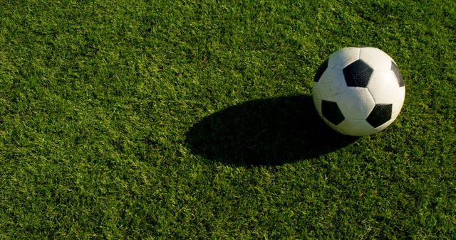 Soccer ball rests on a lush green field, with copy space. Outdoor sports equipment signals readiness for a game or practice.