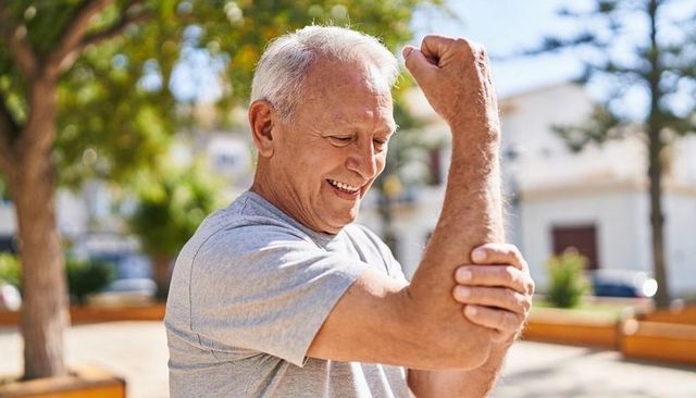 Senior man stretching and massaging elbow outdoors smiling promoting active healthy aging