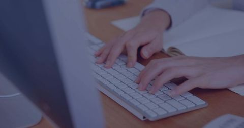 Close-up professional hands typing on slim white keyboard at minimalist office desk with papers