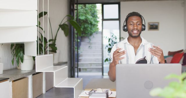 Man wearing headphones participating in video conference in a stylish and modern home office. Suitable for illustrating remote work, virtual communication, and online meetings. Ideal for websites, blogs, and articles focused on telecommuting, digital collaboration, and home office setups.