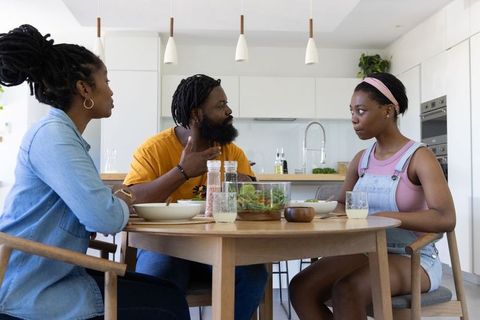 Parents discussing with teen daughter while sharing meal at modern kitchen table