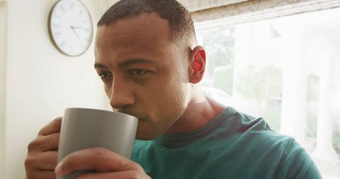 Reflective man drinking coffee in sunlit kitchen
