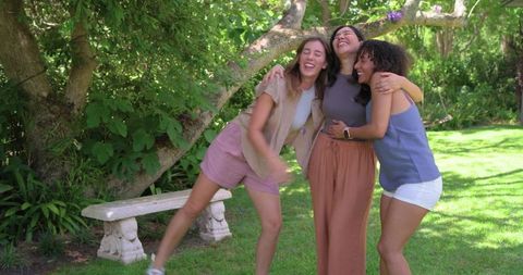 Diverse friends laughing and hugging under flowering tree in sunlit backyard garden
