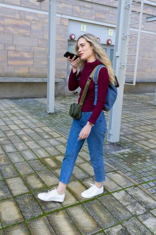 Young woman walking and speaking into smartphone with backpack in urban plaza