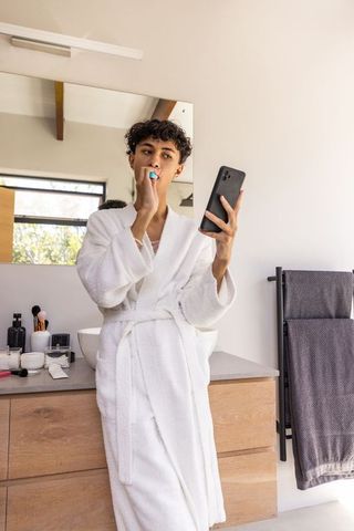 Young Man in Bathrobe Brushing Teeth and Using Smartphone
