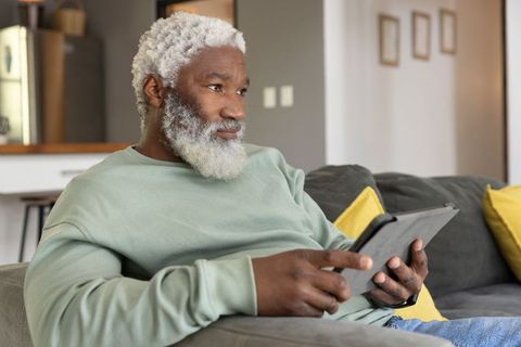 Senior african american man relaxing on couch holding tablet, calm thoughtful lifestyle