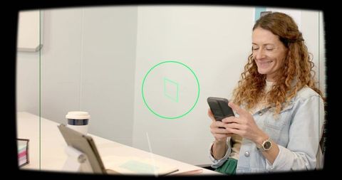 Woman smiling while using smartphone at modern minimalist office desk with tablet