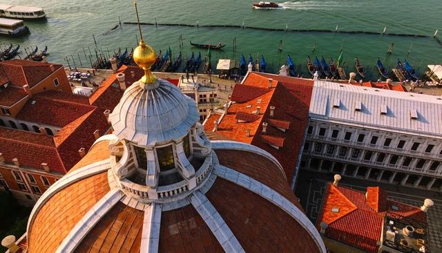Sunlit venetian cupola overlooking grand canal with gondolas and red rooftops aerial view