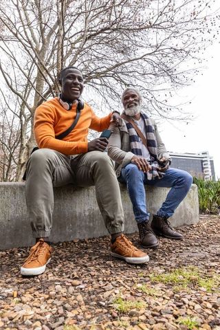 African american friends laughing on urban bench, multigenerational bonding in park