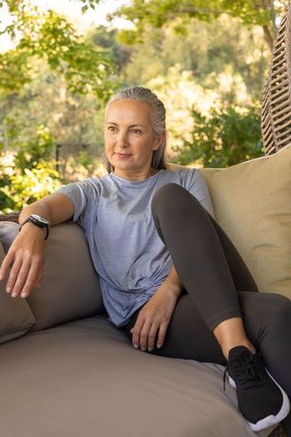 Mature woman relaxing on sunlit patio lounge in garden wearing casual activewear