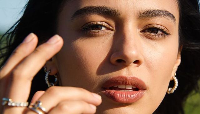 Sunlit closeup woman touching face showcasing hoop earrings and rings, natural makeup