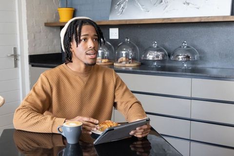 African american man enjoying latte and croissant while using tablet at cozy modern cafe